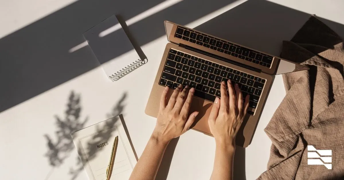 Overhead view of hands typing on a laptop with stationery items nearby, depicting the work environment of a freelance web developer following a 7-step guide to success.
